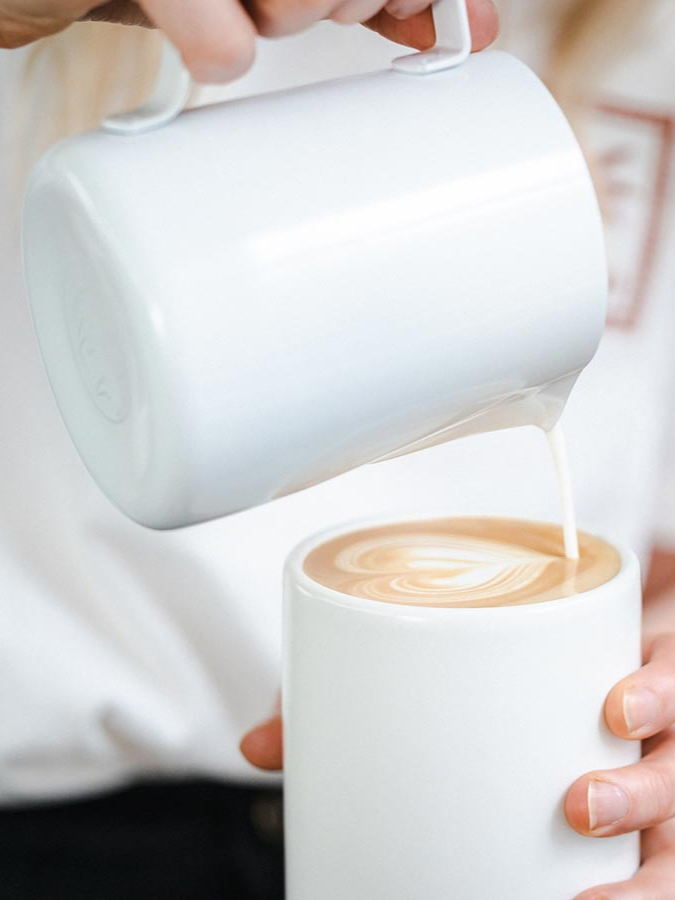 Milchkännchen von Rhino, Milch wird in einen Becher Kaffee gegossen