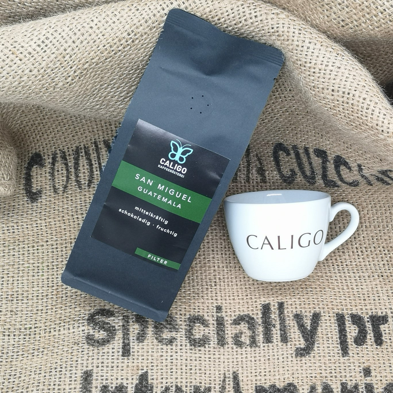 Caligo San Miguel Guatemala mittelkräftig, schokoladig, fruchtig Filterkaffee in schwarzer Tüte neben Caligo Porzellanbecher auf Kaffeesack